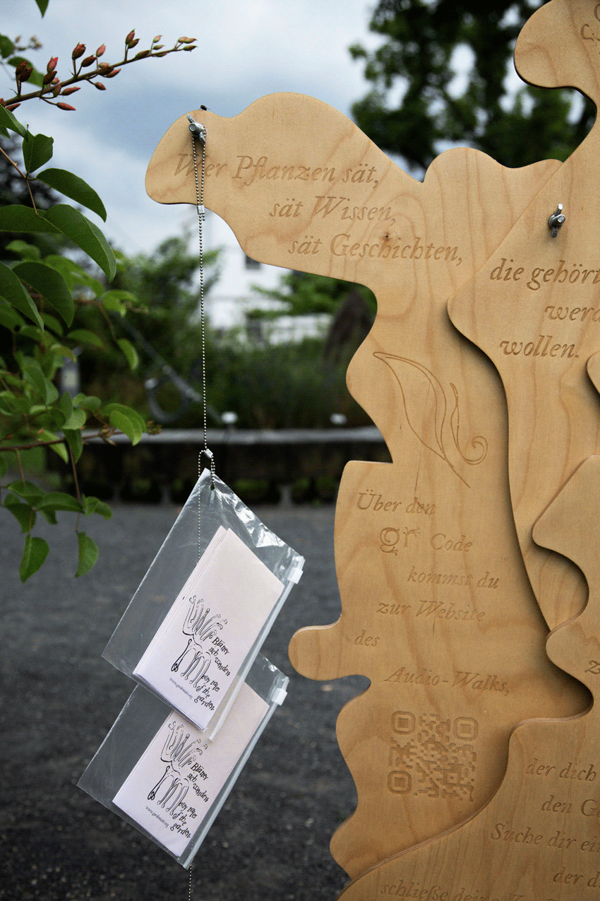 Hozskulptur mit eingravierter Schrift an der zwei Broschüren mit Text hängen